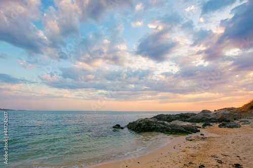 summer vacation landscape by the sea at sunrise. calm water washes sandy beach. dramatic clouds above horizon in morning light on the sky