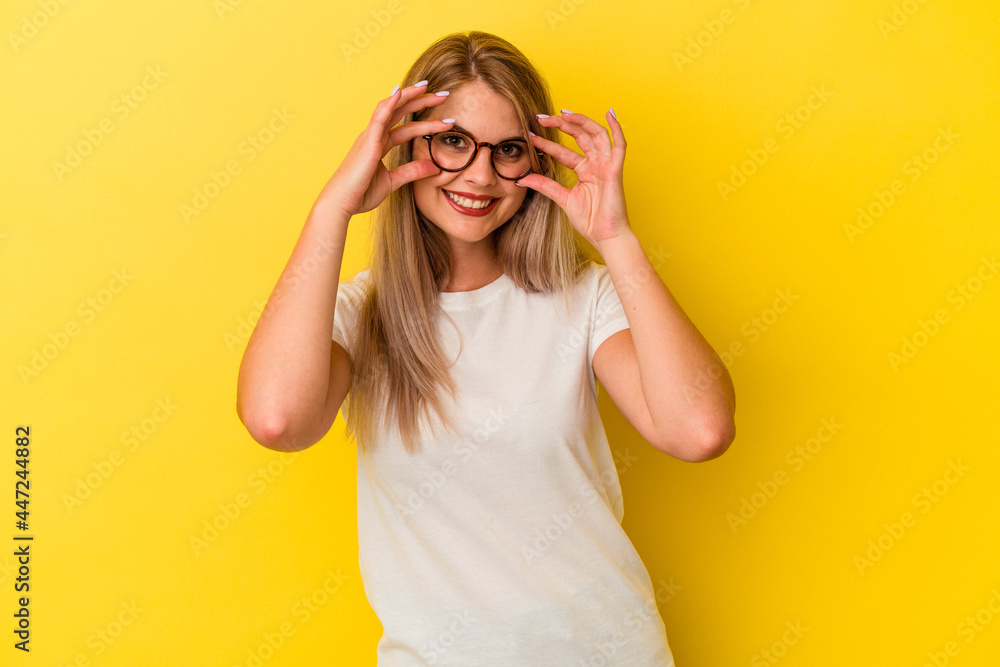 Young russian woman isolated on yellow background showing okay sign over eyes Young russian woman isolated on yellow background showing okay sign over eyes