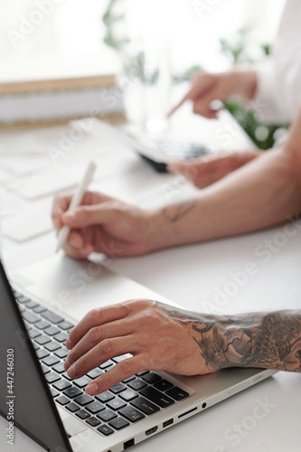 Close-up of man sitting at the table and working on laptop, he typing documents online at office