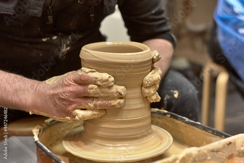 Hands of a ceramist in the process of making a large vase of light clay on a potter s wheel