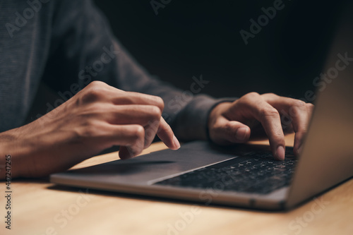 Closeup of a man using a laptop computer on the wooden table, searching, browsing, social media, message, email, internet digital marketing, online shopping..