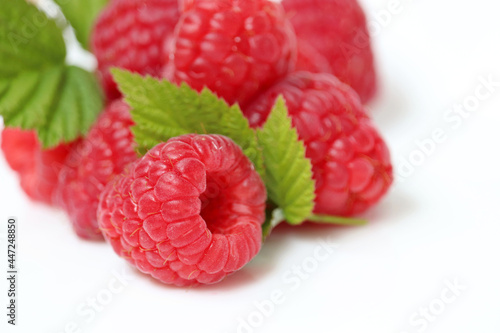 Red raspberry with green leaves on white background. Pile of ripe berries close up, summer crop
