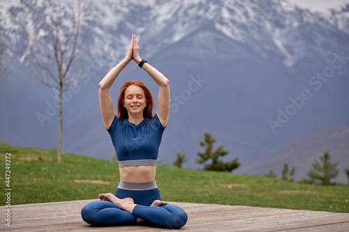Redhead Woman Exercise outdoors. Fit Female practicing yoga pose, keep balance, body vital zen meditation in nature, mountains Landscape outdoor in the background. Healthy lifestyle