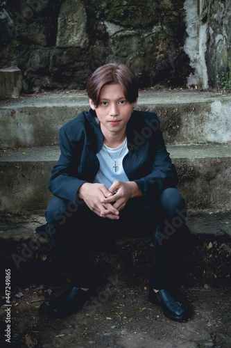 A handsome and fashionable young Filipino teenager that looks like a kpop idol sitting on concrete steps photo