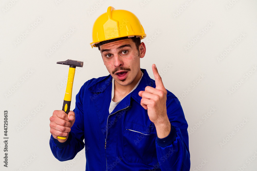 Young caucasian worker man holding a hammer isolated on white background having an idea, inspiration concept.