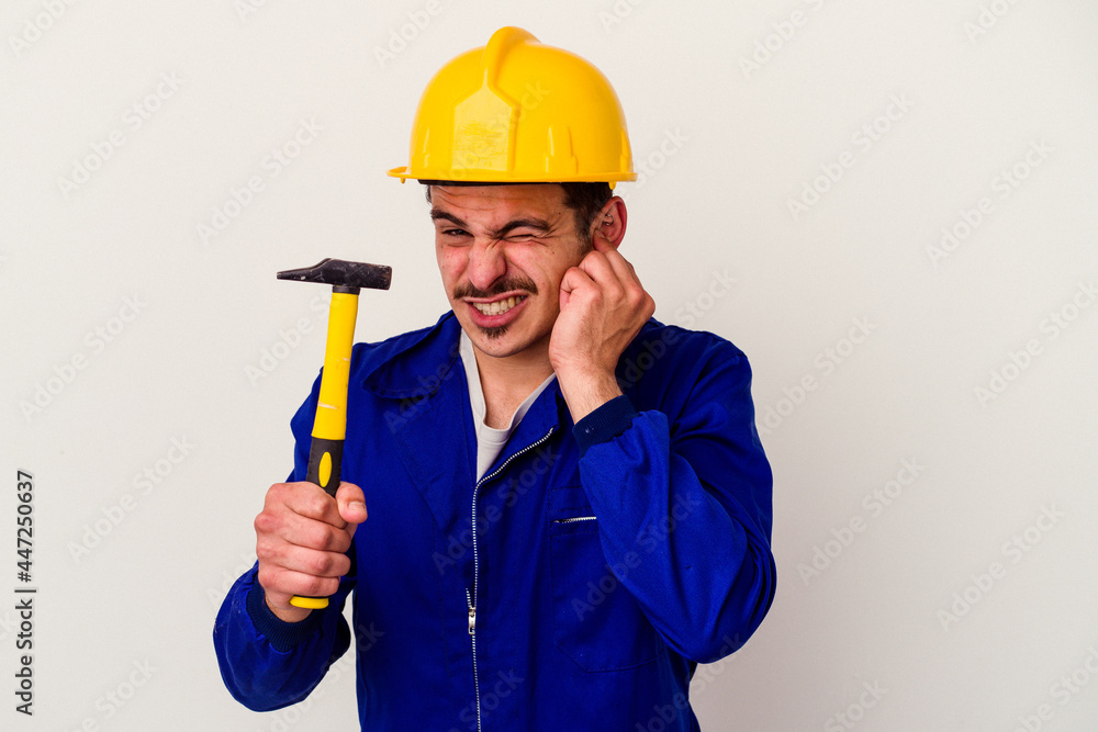 Young caucasian worker man holding a hammer isolated on white background covering ears with hands. Young caucasian worker man holding a hammer isolated on white background covering ears with hands.