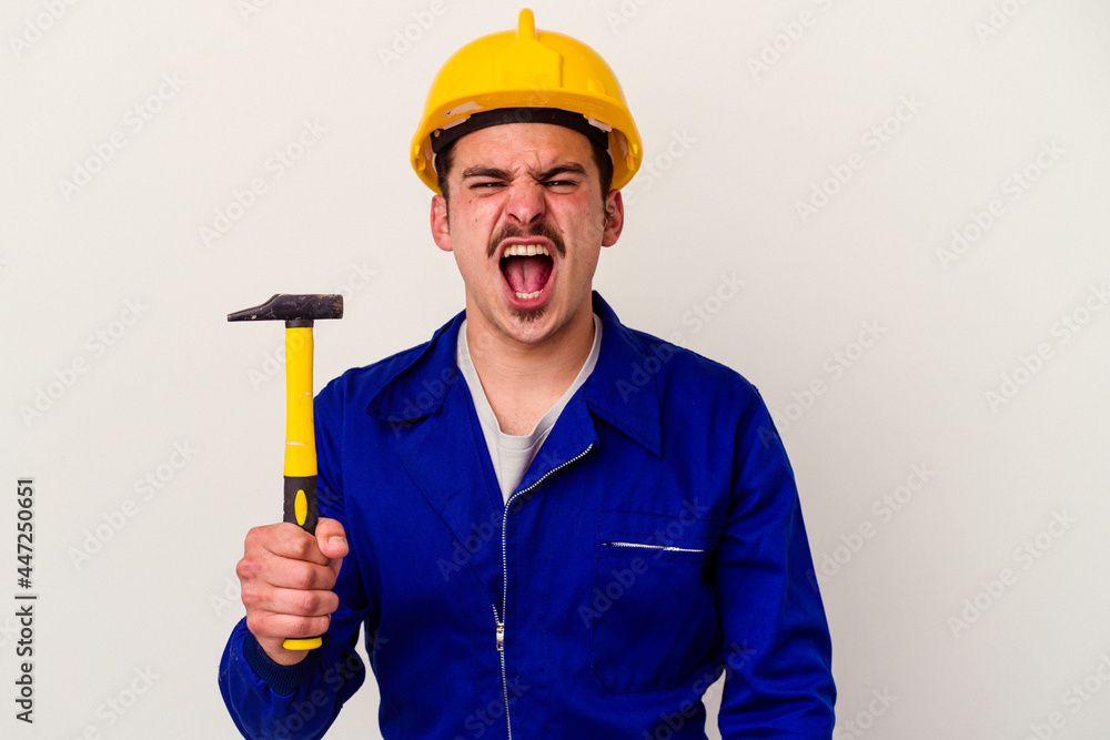 Young caucasian worker man holding a hammer isolated on white background screaming very angry and aggressive. Young caucasian worker man holding a hammer isolated on white background screaming very angry and aggressive.
