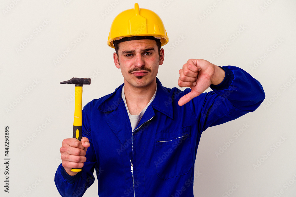 Young caucasian worker man holding a hammer isolated on white background showing a dislike gesture, thumbs down. Disagreement concept. Young caucasian worker man holding a hammer isolated on white background showing a dislike gesture, thumbs down. Disagreement concept.