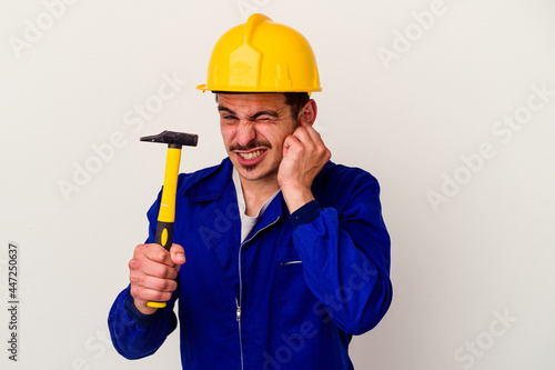 Young caucasian worker man holding a hammer isolated on white background covering ears with hands.