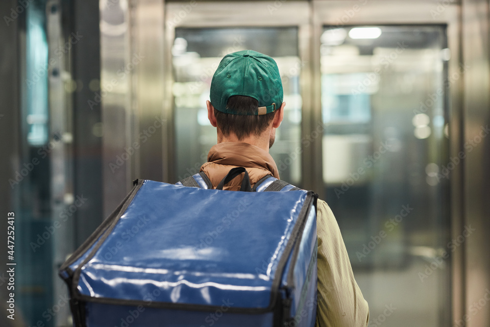 Back view at delivery guy wearing freezer bag while entering office building, copy space Back view at delivery guy wearing freezer bag while entering office building, copy space