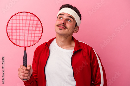 Young caucasian man playing badminton isolated on pink background dreaming of achieving goals and purposes © Asier