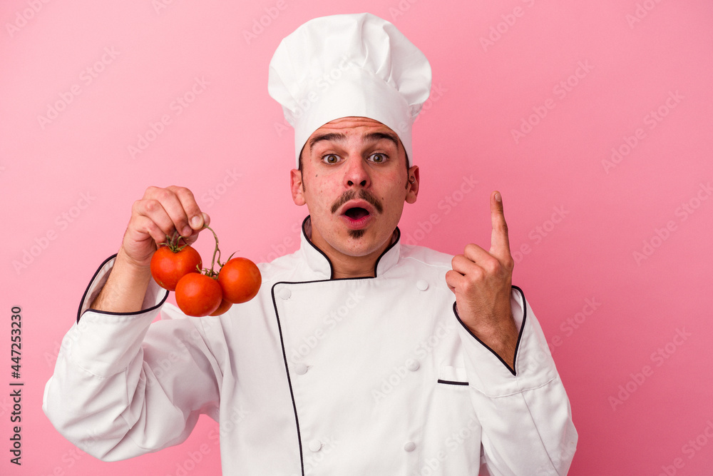 Young caucasian chef man holding tomatoes isolated on pink background having some great idea, concept of creativity. Young caucasian chef man holding tomatoes isolated on pink background having some great idea, concept of creativity.