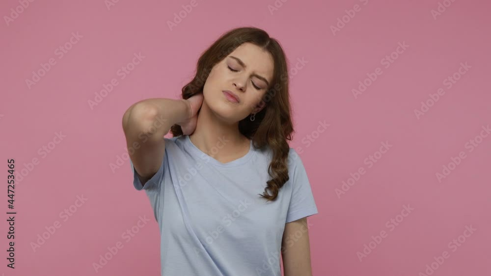 Sick young teenager in casual attire suffering intense pain in back neck, touching sore stiff muscles and frowning from ache, feeling overworked. Indoor studio shot isolated over pink background. Sick young teenager in casual attire suffering intense pain in back neck, touching sore stiff muscles and frowning from ache, feeling overworked. Indoor studio shot isolated over pink background.