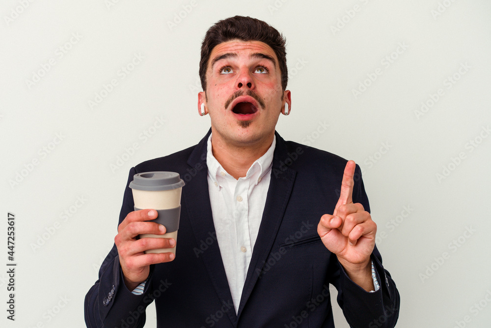 Young business caucasian man wearing wireless headphones and holding take way coffee isolated on white background pointing upside with opened mouth. Young business caucasian man wearing wireless headphones and holding take way coffee isolated on white background pointing upside with opened mouth.