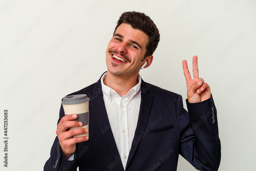 Young business caucasian man wearing wireless headphones and holding take way coffee isolated on white background joyful and carefree showing a peace symbol with fingers. Young business caucasian man wearing wireless headphones and holding take way coffee isolated on white background joyful and carefree showing a peace symbol with fingers.