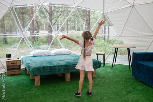 Fototapeta Cute girl looking through transparent bell tent with comfortable bed in forest,