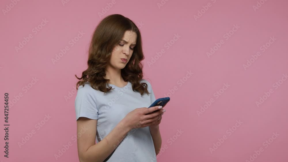 Positive smiling woman of young age with wavy hair in casual clothing holding phone, chatting friend, keeping friendly conversation. Indoor studio shot isolated over pink background. Positive smiling woman of young age with wavy hair in casual clothing holding phone, chatting friend, keeping friendly conversation. Indoor studio shot isolated over pink background.