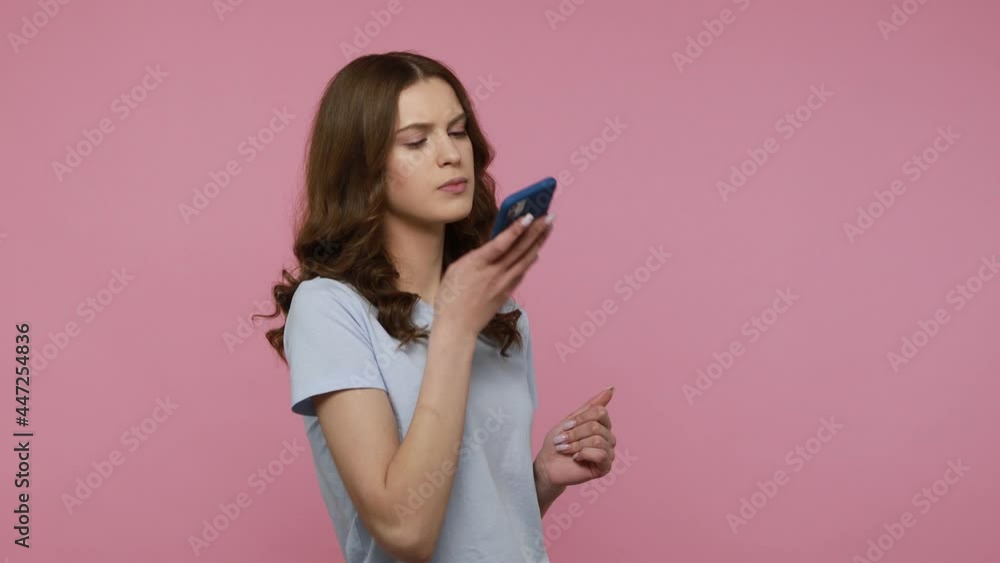 Attractive woman in blue T-shirt making voice records on mobile phone, talking to smart device, using virtual assistant for online search. Indoor studio shot isolated over pink background. Attractive woman in blue T-shirt making voice records on mobile phone, talking to smart device, using virtual assistant for online search. Indoor studio shot isolated over pink background.