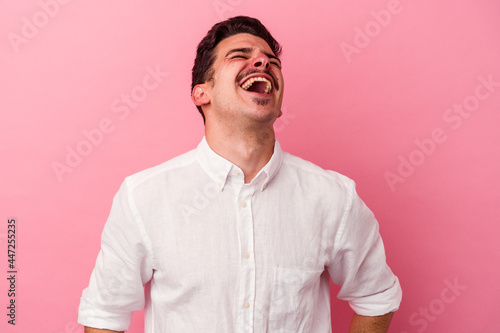 Young caucasian man isolated on pink background relaxed and happy laughing, neck stretched showing teeth.