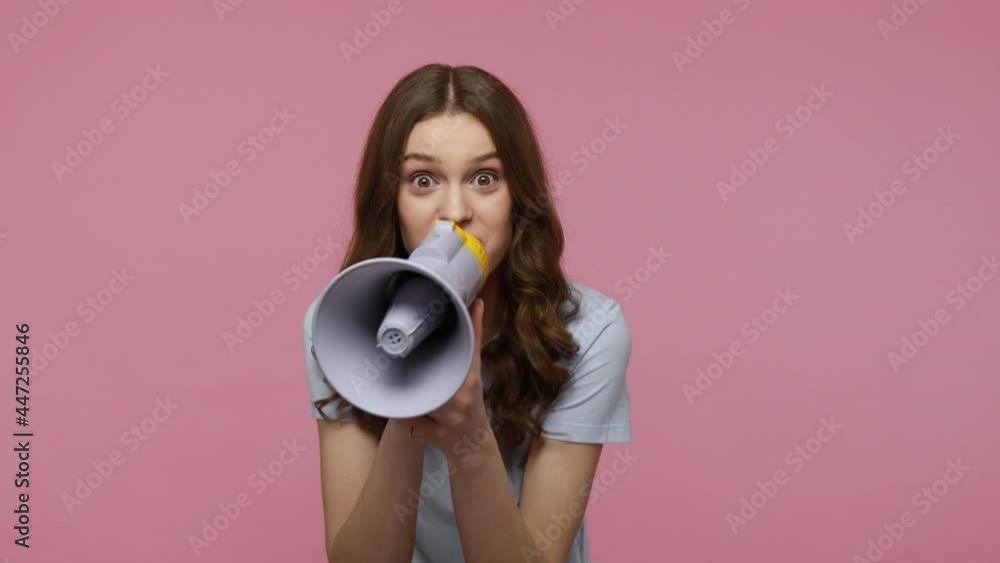 Happy teenager girl wears casual T-shirt uses loudspeaker for proclaiming breaking news or announcing advertisement, yelling with excited expression. Indoor studio shot isolated over pink background. Happy teenager girl wears casual T-shirt uses loudspeaker for proclaiming breaking news or announcing advertisement, yelling with excited expression. Indoor studio shot isolated over pink background.