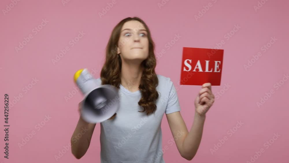 Teenager girl promoter in T-shirt announcing news in megaphone about discounts, holding card with sale inscription in hand, advertising. Indoor studio shot isolated over pink background. Teenager girl promoter in T-shirt announcing news in megaphone about discounts, holding card with sale inscription in hand, advertising. Indoor studio shot isolated over pink background.