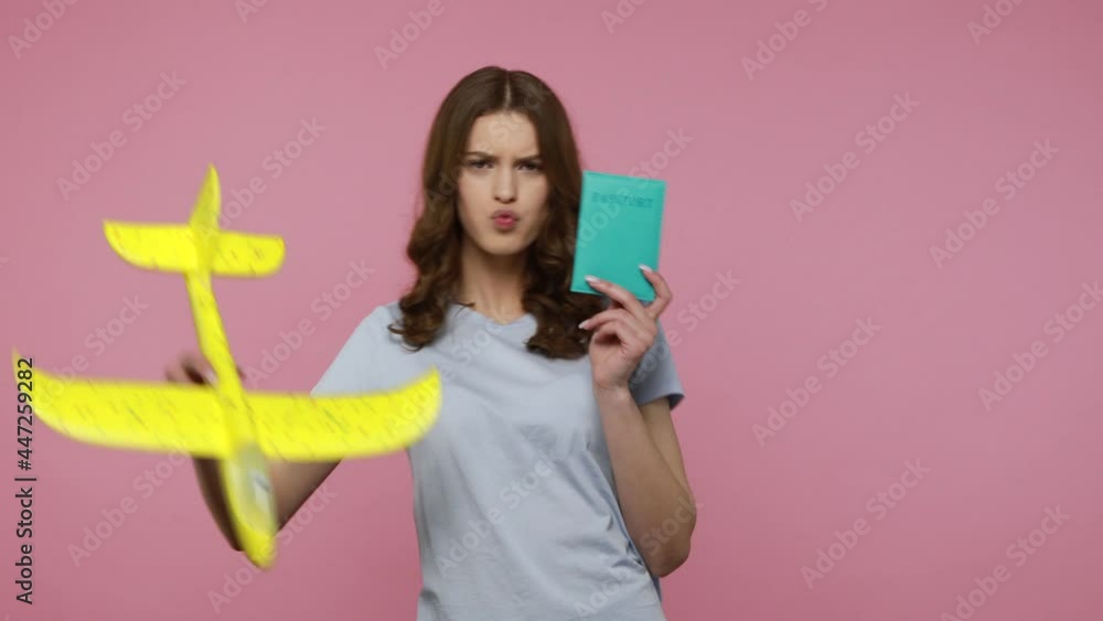Amazing carefree happy teenager girl in casual T-shirt playing with plane and holding passport, planning trip abroad on air transport. Indoor studio shot isolated over pink background. Amazing carefree happy teenager girl in casual T-shirt playing with plane and holding passport, planning trip abroad on air transport. Indoor studio shot isolated over pink background.