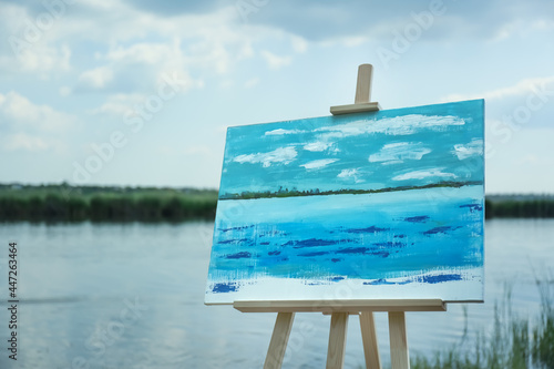 Wooden easel with unfinished painting near lake