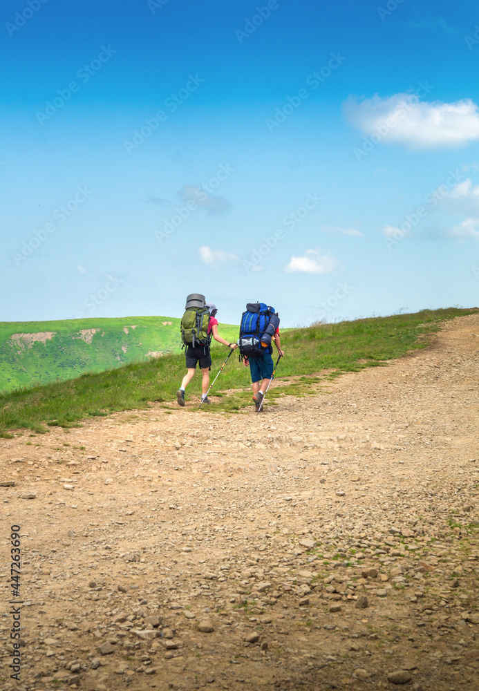 Two tourists with backpacks are walking along the stone road to the top of the mountain. Summer hiking in the mountains