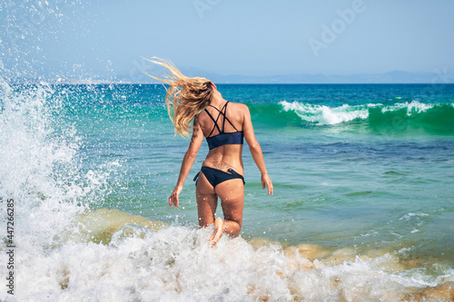 Chica rubia joven y sexy en bikini jugando con las olas al romper en las rocas en la playa de Punta Paloma, Tarifa, Cádiz, Andalucía, España. © inigolaitxu