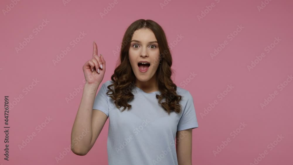 Inspired cheerful nice-looking teenager girl in T-shirt pointing finger up having excellent idea, excited about genius plan, creative thought. Indoor studio shot isolated over pink background. Inspired cheerful nice-looking teenager girl in T-shirt pointing finger up having excellent idea, excited about genius plan, creative thought. Indoor studio shot isolated over pink background.