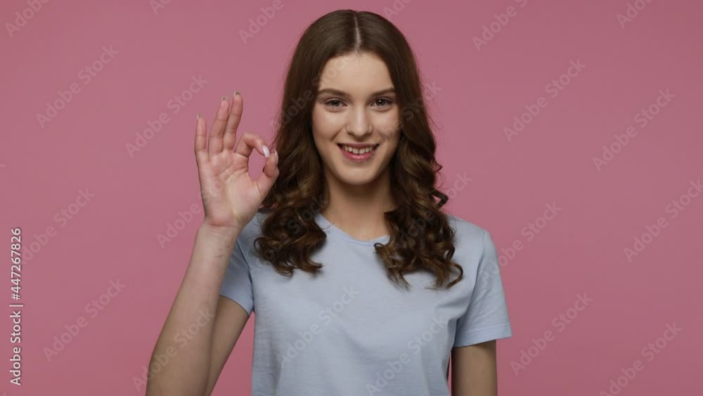 I am ok, everything is fine! Dark haired teenager girl in T-shirt showing okay sing to camera and winking her eye, approving gesture. Indoor studio shot isolated over pink background. I am ok, everything is fine! Dark haired teenager girl in T-shirt showing okay sing to camera and winking her eye, approving gesture. Indoor studio shot isolated over pink background.