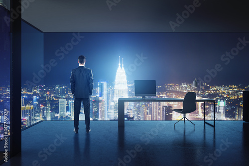 Success concept with businessman back view in high floor stylish office with night city skyscrapers view through mesh walls.