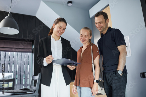 Waist up portrait of happy young couple talking to real estate agent while buying new house, copy space