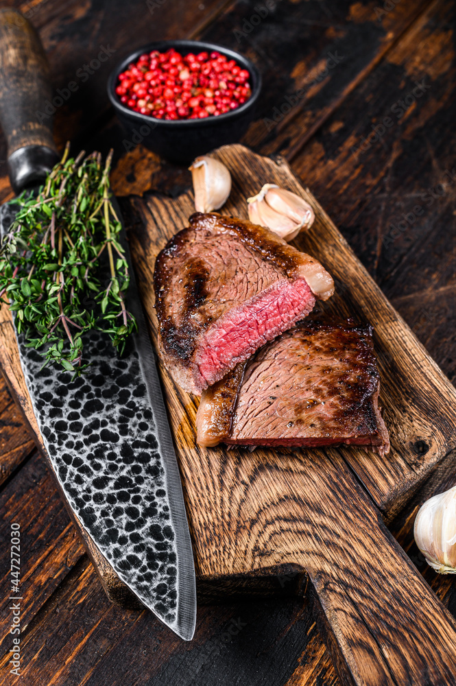 Cut fried rump cap or brazilian picanha beef meat steak on a wooden board. Dark wooden background. Top view