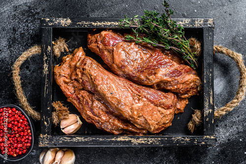 Raw marinated brisket steaks in a wooden tray with herbs. Black background. Top view