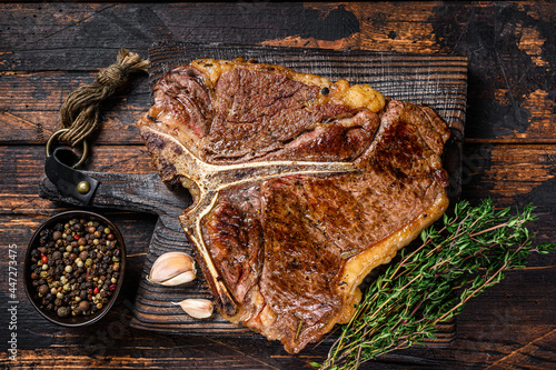 Roast t-bone or porterhouse beef meat Steak on a wooden cutting board. Dark wooden background. Top view photo