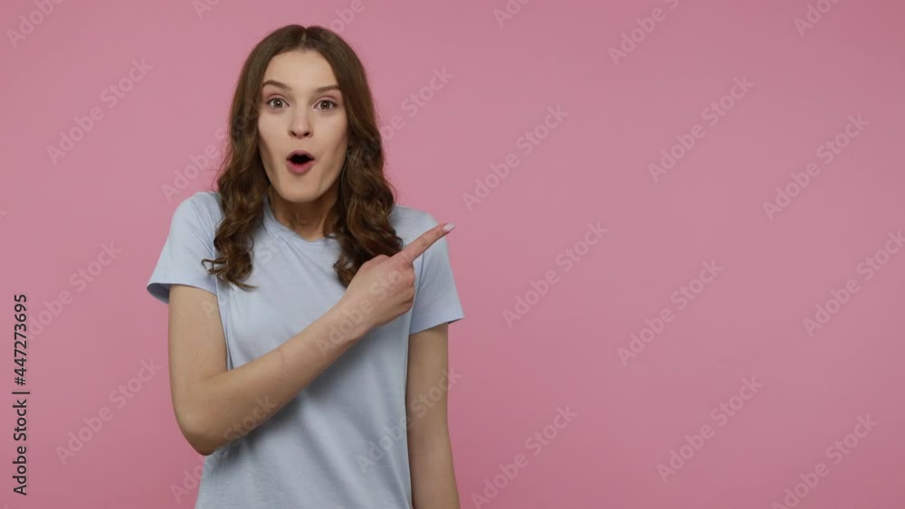 Amazed female with wavy hair holding copy space on palm and looking surprised, pointing at workspace for advertisement, empty place for promotion. Indoor studio shot isolated over pink background. Amazed female with wavy hair holding copy space on palm and looking surprised, pointing at workspace for advertisement, empty place for promotion. Indoor studio shot isolated over pink background.