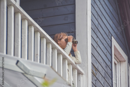 the child girl looks through binoculars standing on the balcony of the house