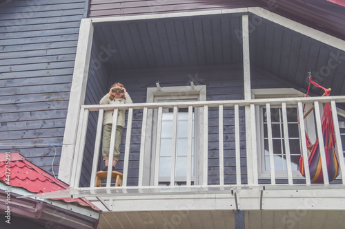 the child girl looks through binoculars standing on the balcony of the house photo