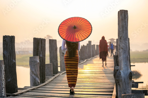 A young Burmese woman wearing traditional clothes with red umbrella at U Bein teak bridge in Mandalay Division. Myanmar. photo