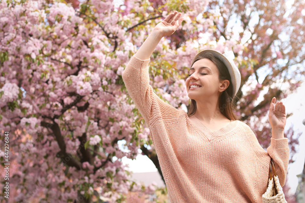 Happy stylish young woman near blossoming sakura tree outdoors. Spring look Happy stylish young woman near blossoming sakura tree outdoors. Spring look