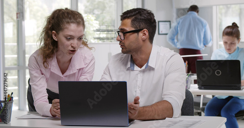 Young cheerful female caucasian and male indian coworkers discussing project strategy in office