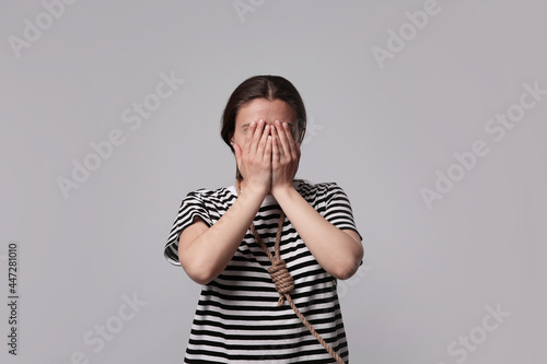 Depressed woman with rope noose on neck against light grey background