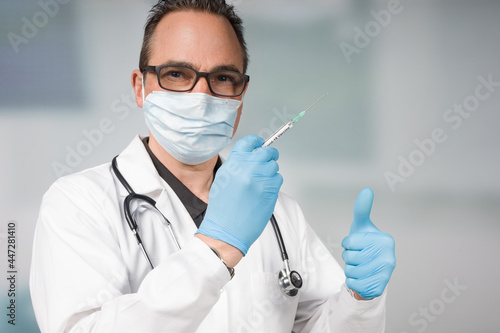 doctor with medical face mask and medical gloves presenting a syringe pulled up with a coronavirus vaccine showing thumbs up