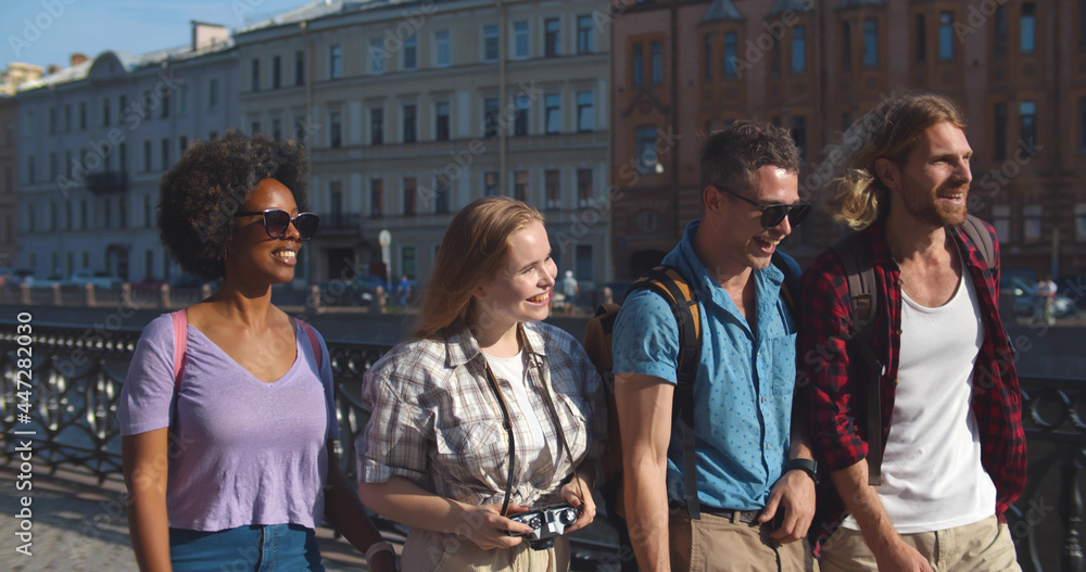 Slider shot of group of diverse friends tourists walking on city embankment Slider shot of group of diverse friends tourists walking on city embankment