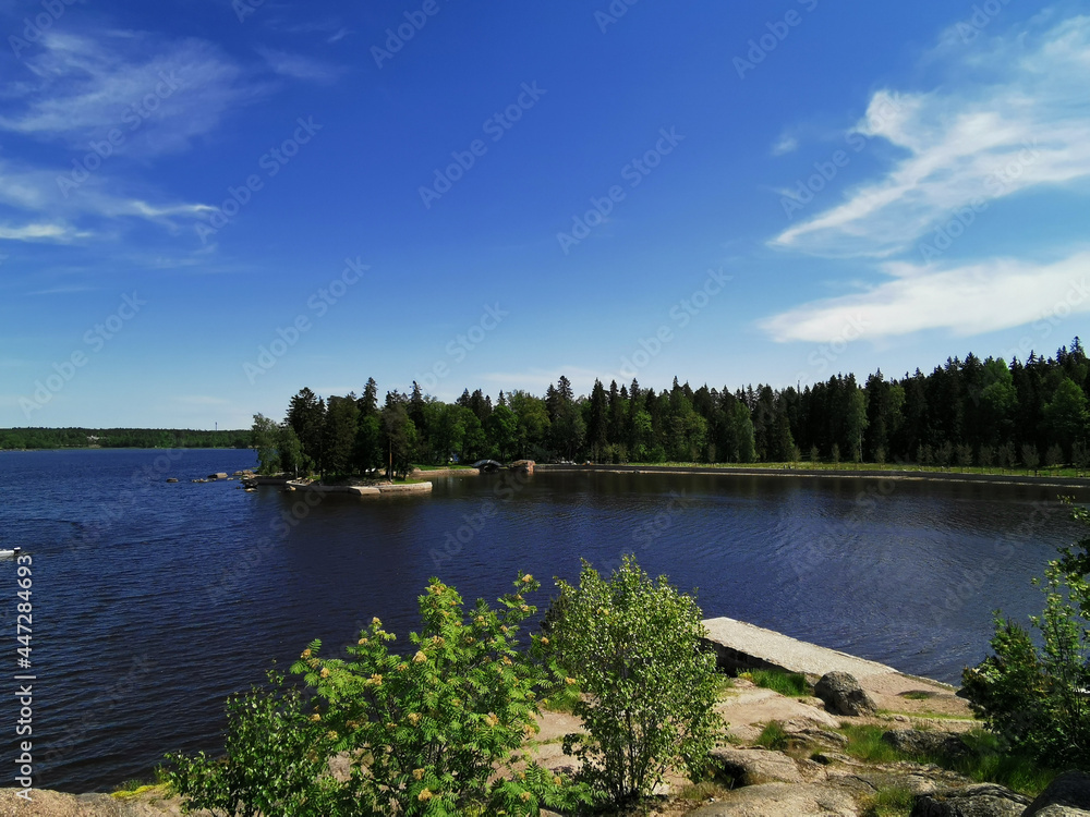 Naklejka premium View from the observation deck on the picturesque shore of the Vyborg Bay in the Monrepos Park of the city of Vyborg against the background of a blue sky with clouds.