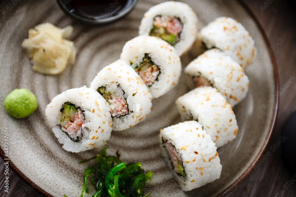 Sushi maki rolls California with crab, cucumber and avocado on a plate with chopsticks, soy sauce, wasabi and ginger. Japanese traditional seafood served for lunch in modern gourmet restaurant Sushi maki rolls California with crab, cucumber and avocado on a plate with chopsticks, soy sauce, wasabi and ginger. Japanese traditional seafood served for lunch in modern gourmet restaurant