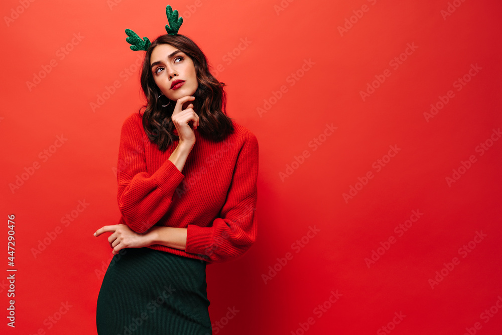 Pensive lady with brunette hair in red sweater and green skirt looking away on isolated backdrop. Woman in cool outfit posing on bright background.. Pensive lady with brunette hair in red sweater and green skirt looking away on isolated backdrop. Woman in cool outfit posing on bright background..