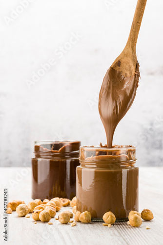 Chocolate cream in glass jar with hazelnuts and dripping spoon, on wooden table photo