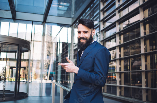 Positive man standing with phone among urban office building